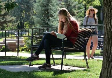 female student with blonde hair and red sweater reading on a bench
